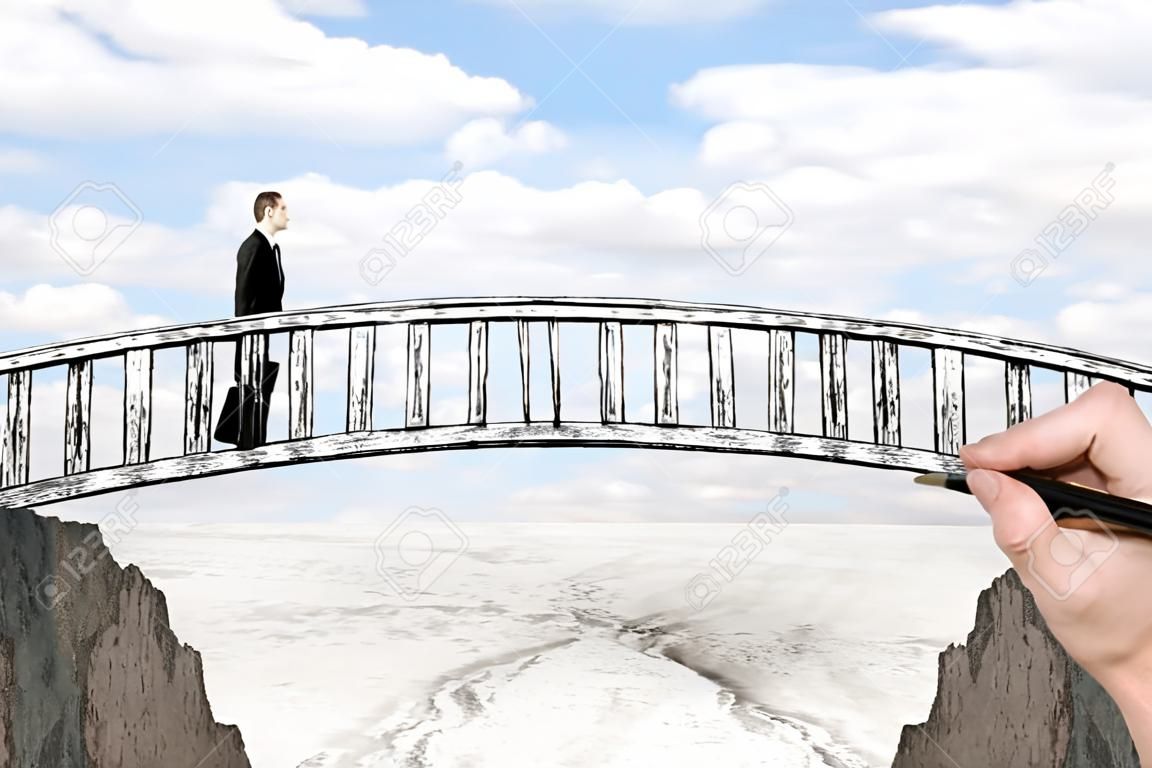 Success concept with hand drawing bridge over gap between two cliffs and businessman walking across it on landscape background