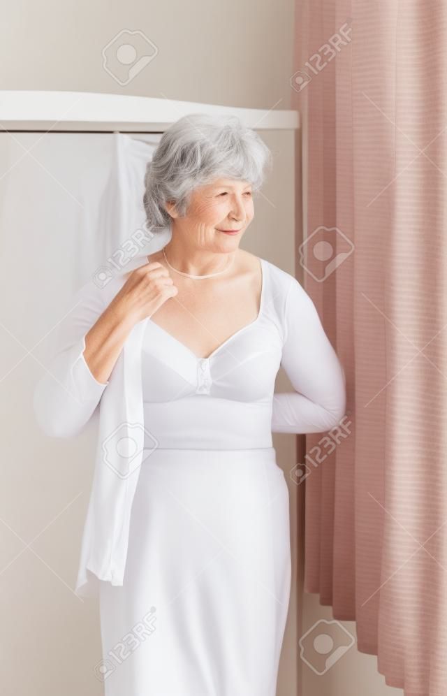 Elderly woman getting dressed putting on a white shirt