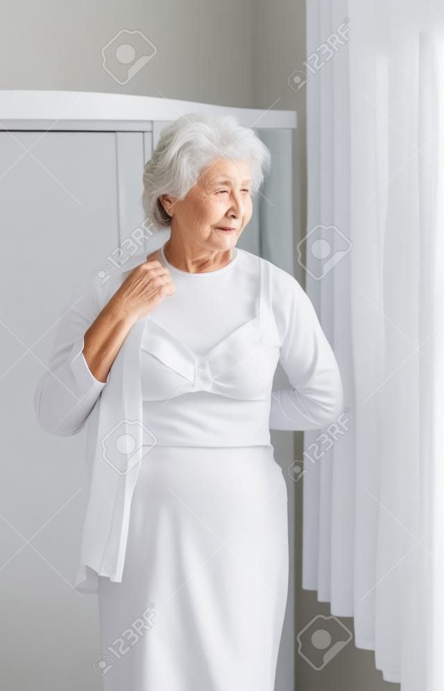 Elderly woman getting dressed putting on a white shirt