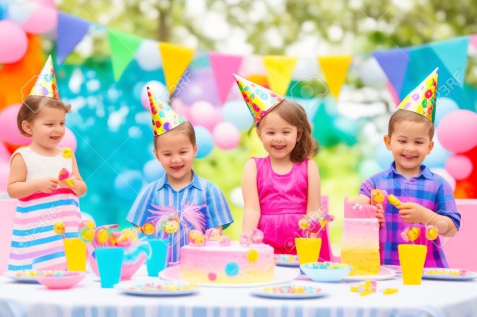 Fiesta de cumpleaños al aire libre para los niños pequeños con pastel de colores