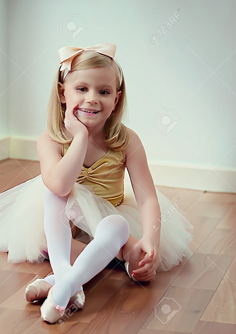Linda niña rubia sentada en tutú de ballet con un lazo en el pelo