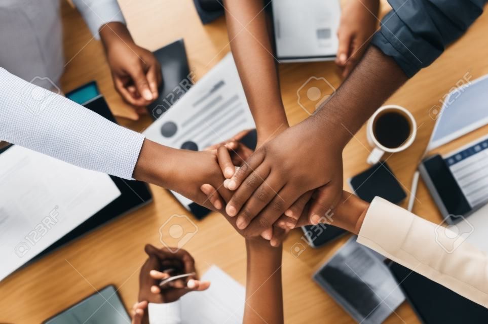 A multiracial team, coworkers put their hand on hand of one another. A sign of a close-knit multicaltural team, top view