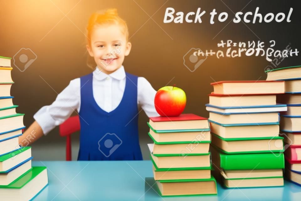 Back to school. Smart school girl reading a book at library. Mathematical formula at blackboard. Table with many books and one green apple. Student. Concept of education