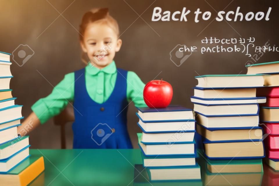 Back to school. Smart school girl reading a book at library. Mathematical formula at blackboard. Table with many books and one green apple. Student. Concept of education