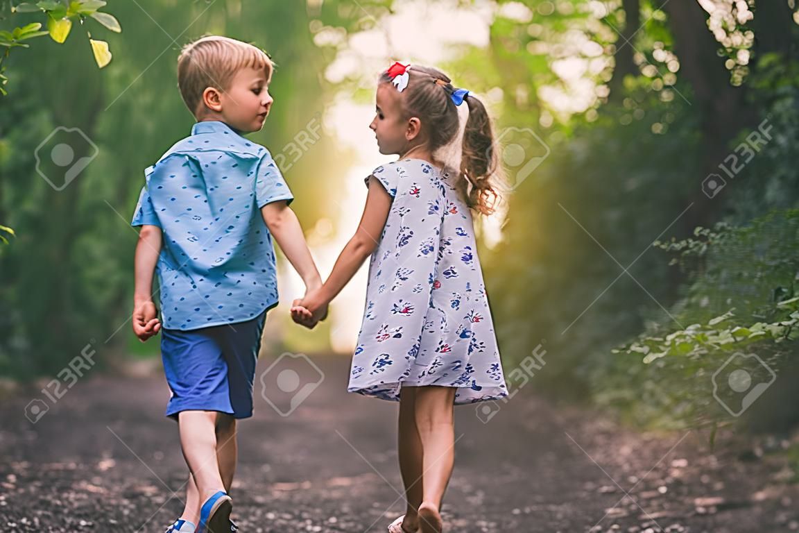 Szczęśliwe dzieci spacerujące na świeżym powietrzu w parku trzymają się za ręce.