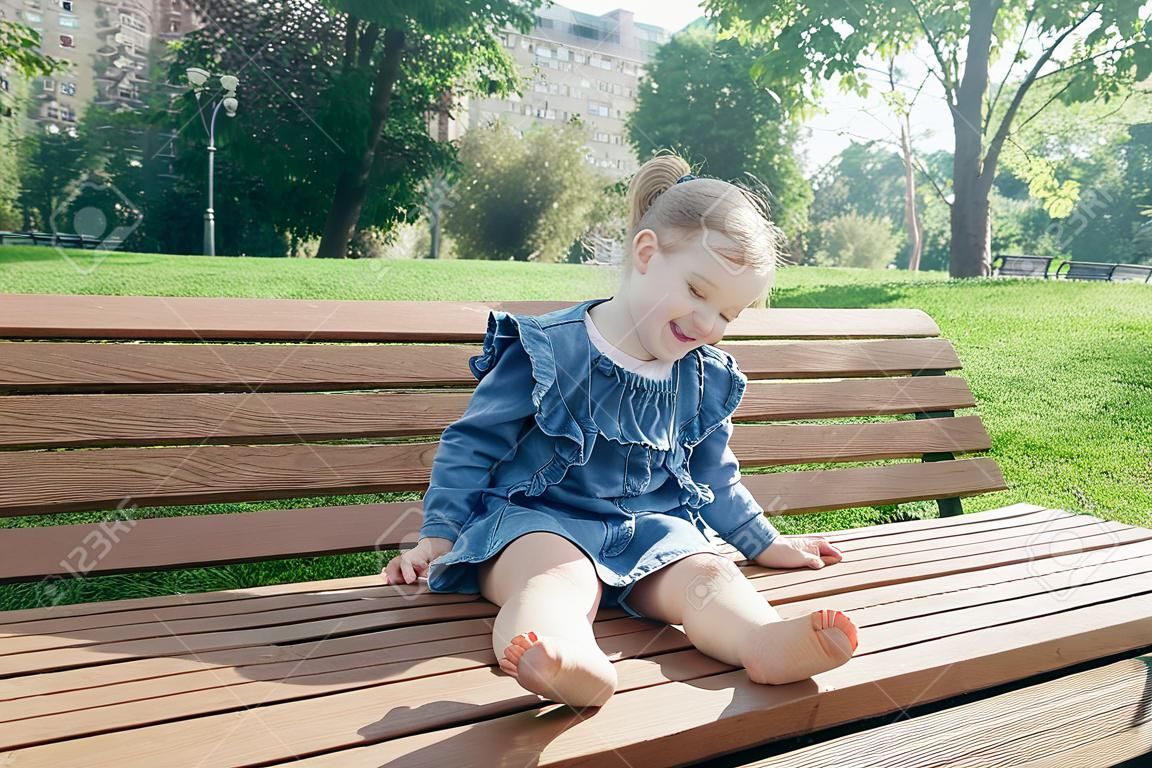 Little girl sitting on the bench and laughing in a city park on a warm sunny day