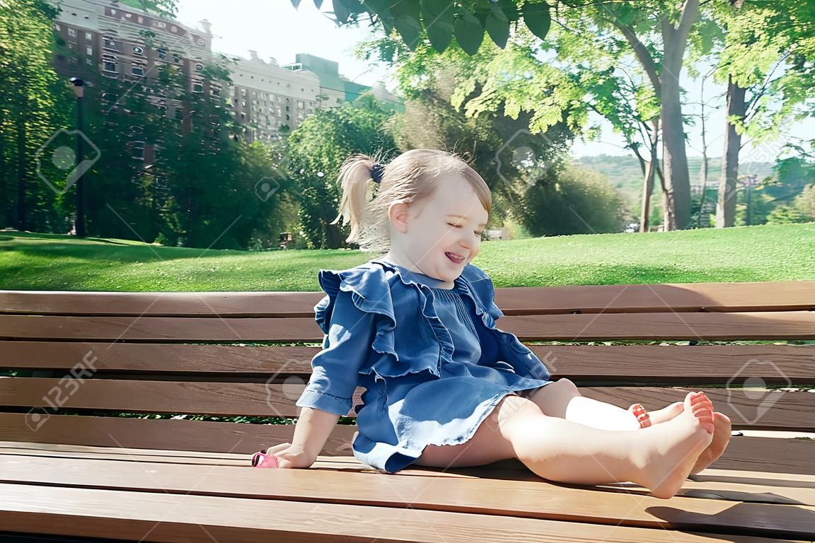 Little girl sitting on the bench and laughing in a city park on a warm sunny day