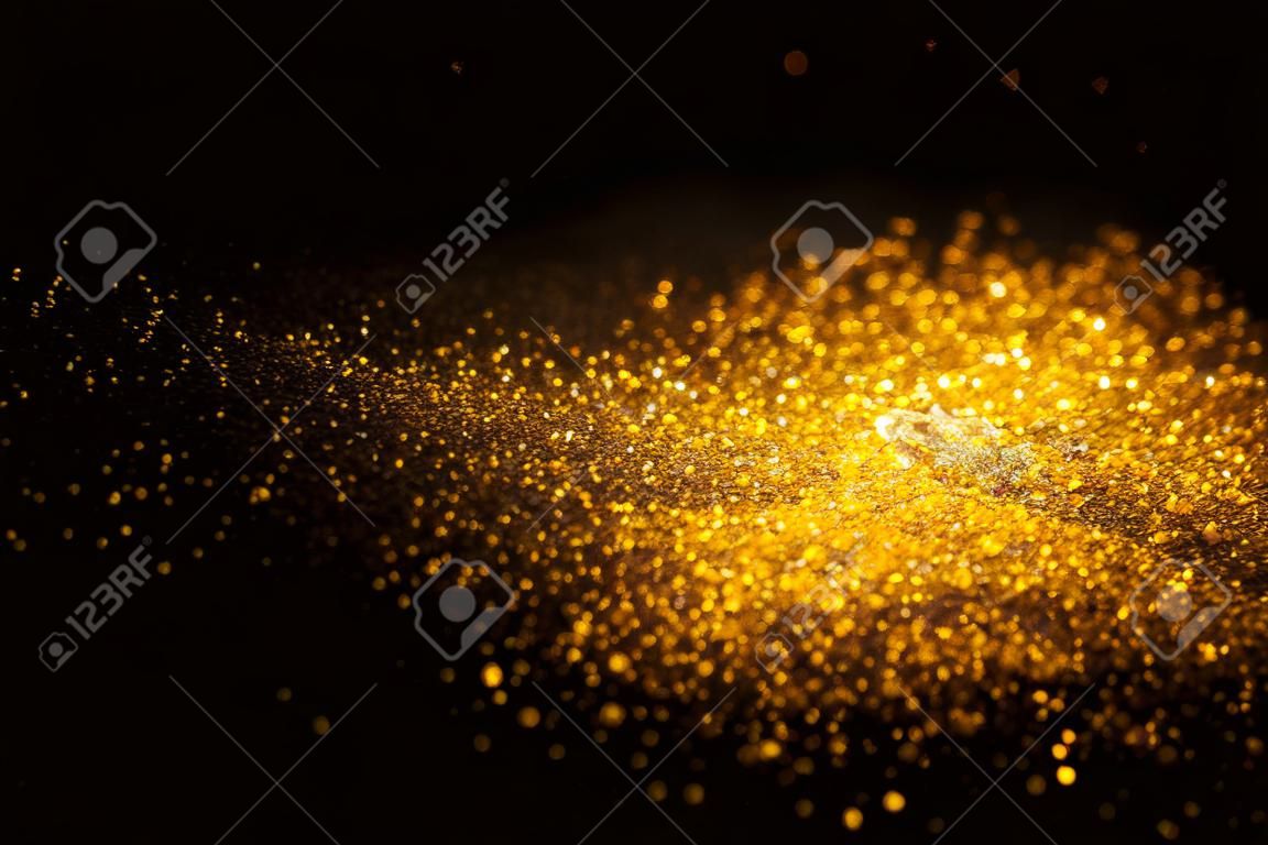 Sprinkle gold glitter dust on a black background with copy space.