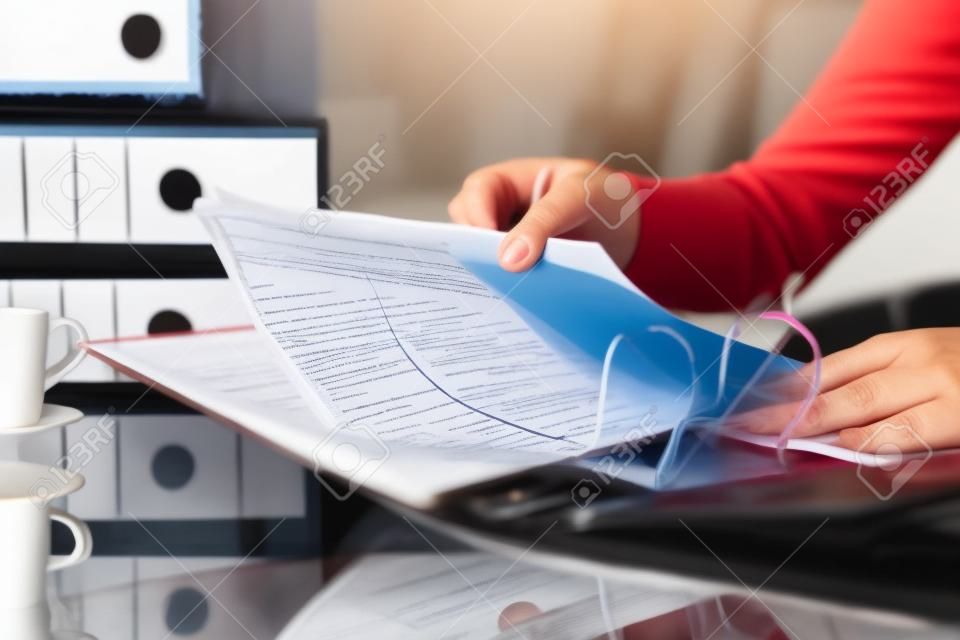 Cerca de las manos de la mujer organizando documentos poniendo archivos en una carpeta en un escritorio en casa