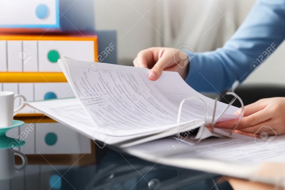Cerca de las manos de la mujer organizando documentos poniendo archivos en una carpeta en un escritorio en casa