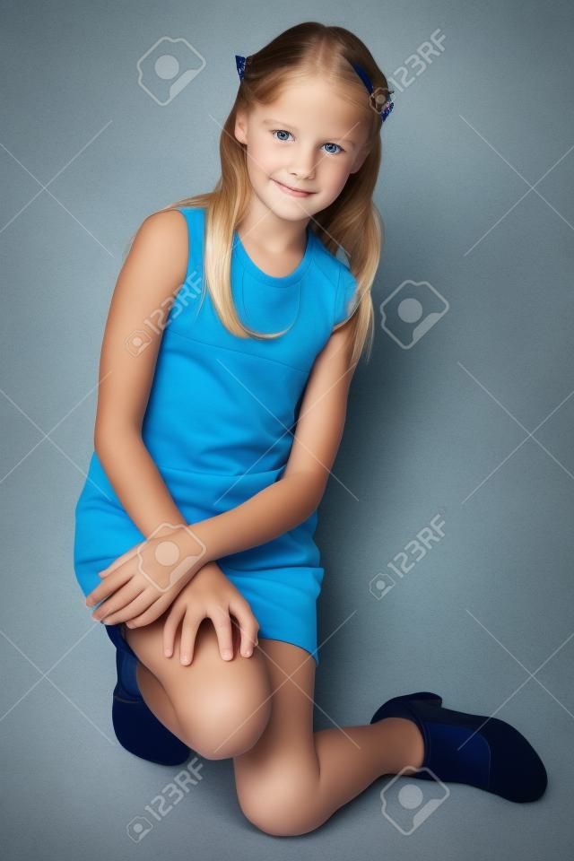 Slender beautiful girl in a striped dress sat on her knee. Pretty happy attractive child in blue tights. The young schoolgirl is 9 years old.