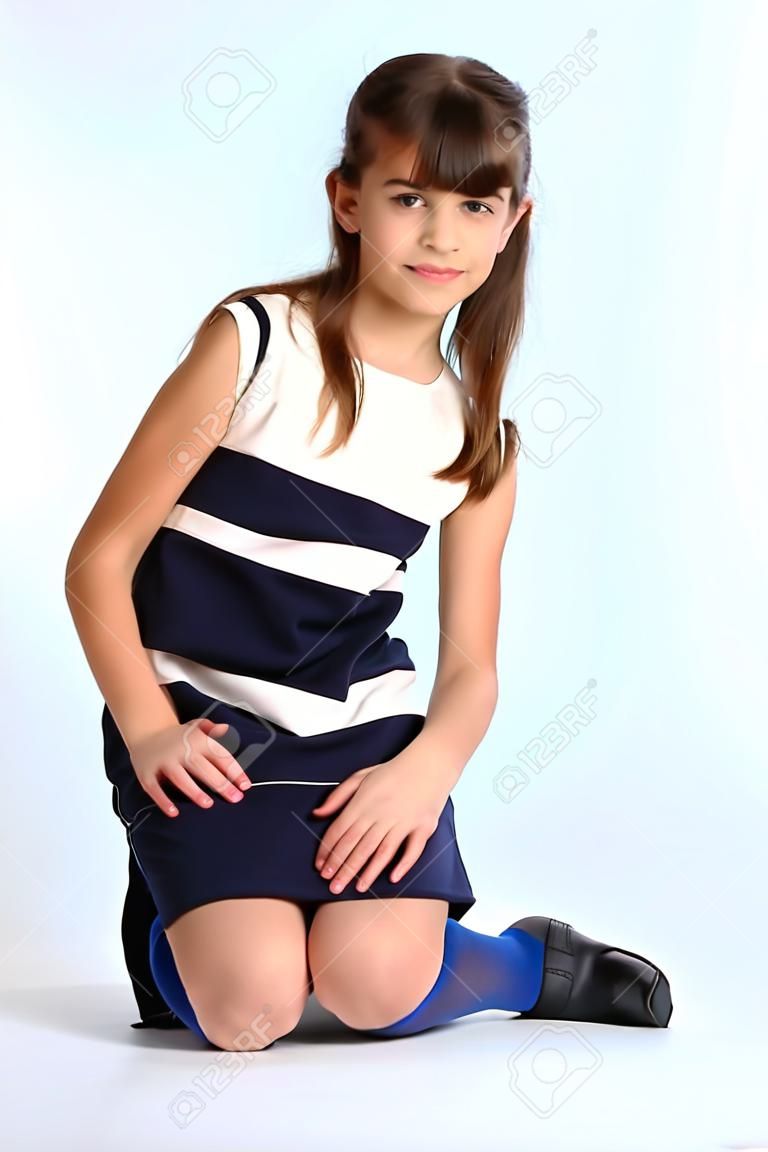 Snella bella ragazza con un vestito a strisce seduto sul suo ginocchio. Bambino attraente abbastanza felice in collant blu. La giovane studentessa ha 9 anni.