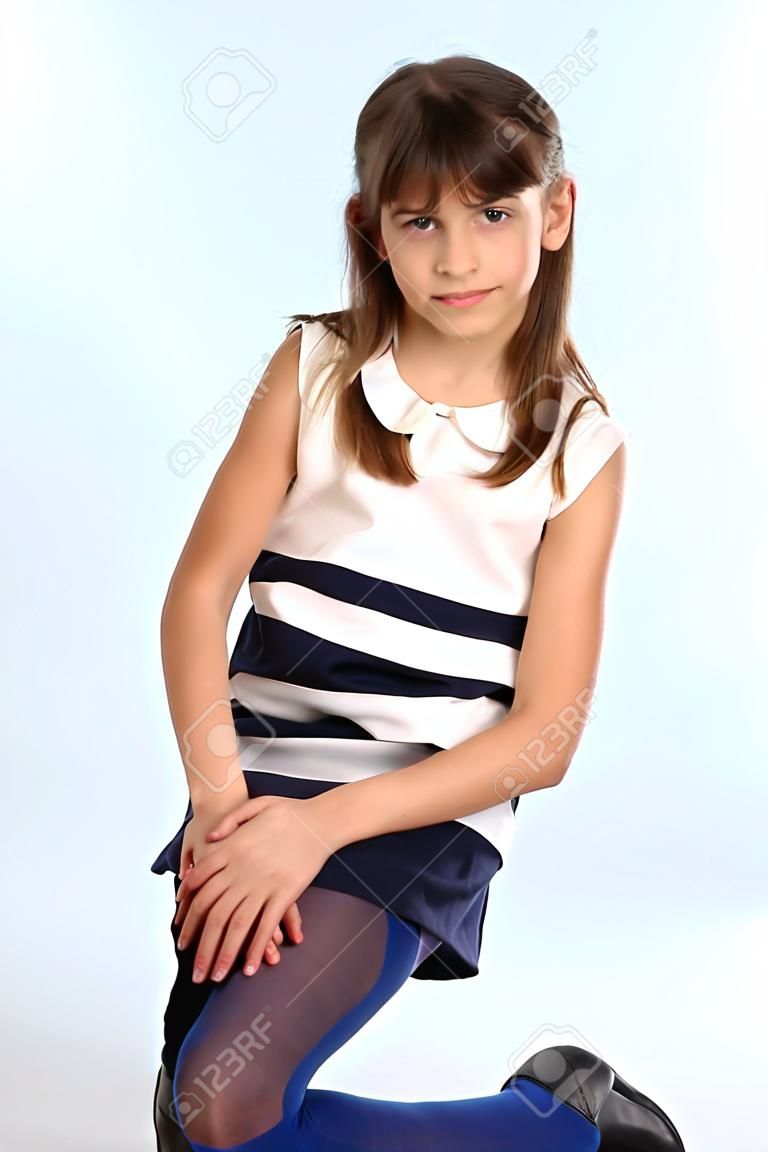 Szczupła, piękna dziewczyna w pasiastej sukience usiadła na kolanie. Całkiem szczęśliwe atrakcyjne dziecko w niebieskich rajstopach. Młoda uczennica ma 9 lat.