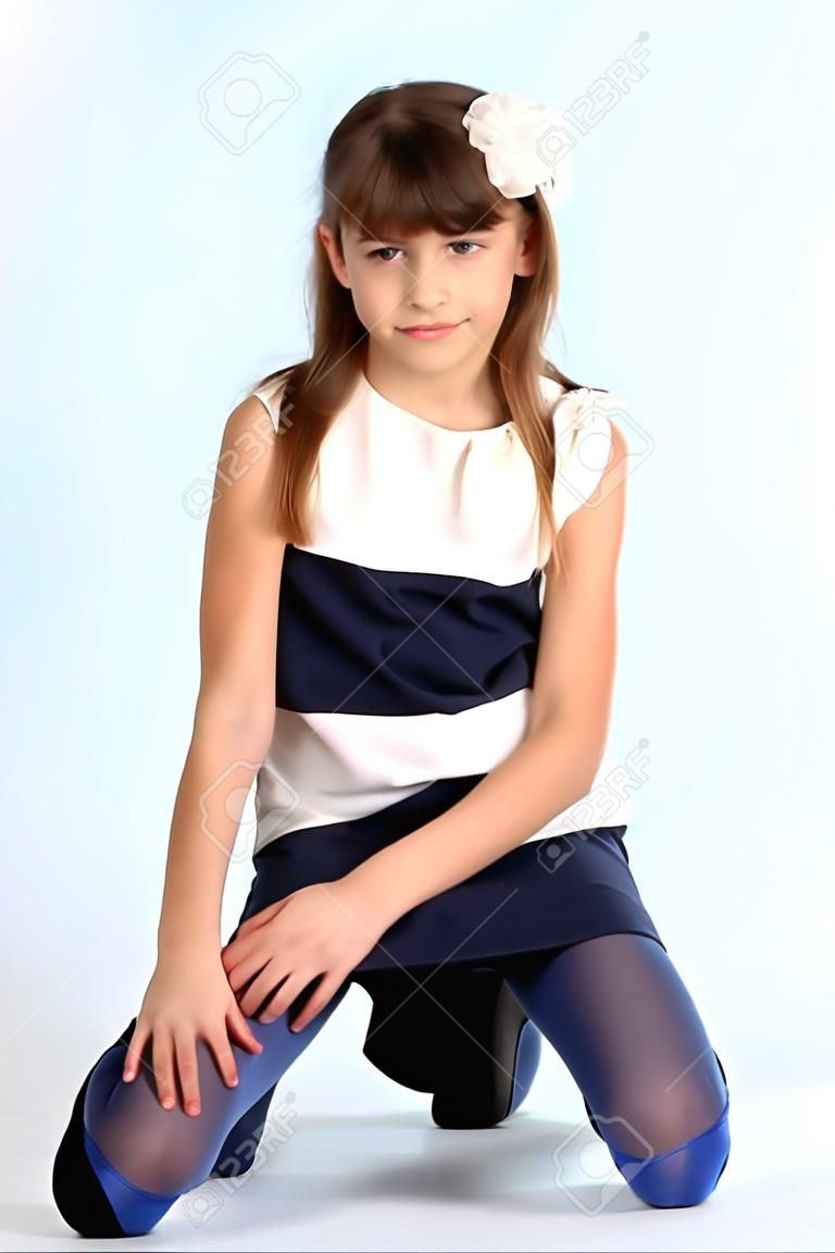 Menina bonita esbelta em um vestido listrado sentou-se em seu joelho. Criança atraente muito feliz em meias azuis. A jovem estudante tem 9 anos de idade.