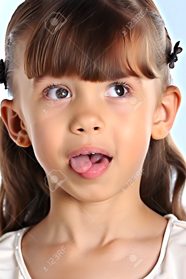 Close-up portrait of a beautiful girl in a white blouse. The cute attractive child teases by pulling her pink tongue and rolling her eyes. The young schoolgirl is 9 years old.