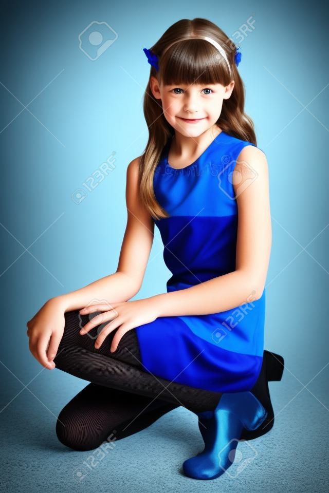 苗条的漂亮女孩，穿着条纹的衣服坐在她的膝盖上。相当蓝色贴身衬衣的愉快的可爱的孩子。年轻的女学生9岁。