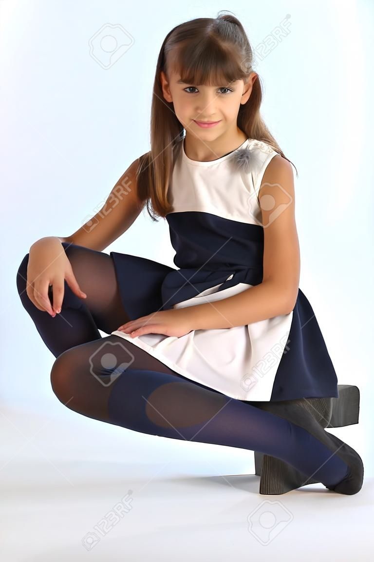 Schlankes schönes Mädchen in einem gestreiften Kleid saß auf ihrem Knie. Ziemlich glückliches attraktives Kind in blauen Strumpfhosen. Das junge Schulmädchen ist 9 Jahre alt.