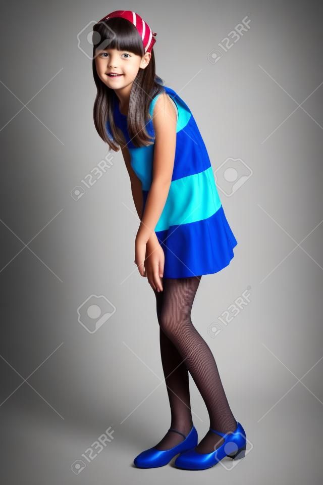 Gyönyörű lány, egy csíkos ruha teljes hosszában áll. Elegáns, vonzó gyermek karcsú testtel és hosszú lábakkal, kék harisnya. A fiatal iskoláslány 9 éves.