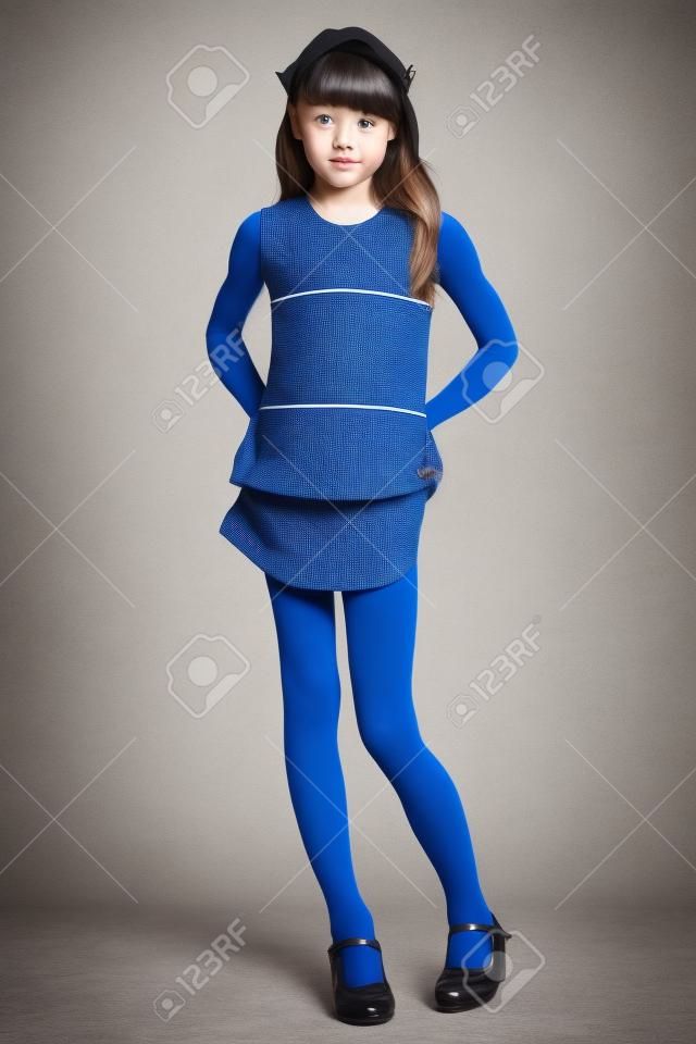 Beautiful girl in a striped dress is standing at full length. Elegant attractive child with a slender body and long legs in blue tights. The young schoolgirl is 9 years old.