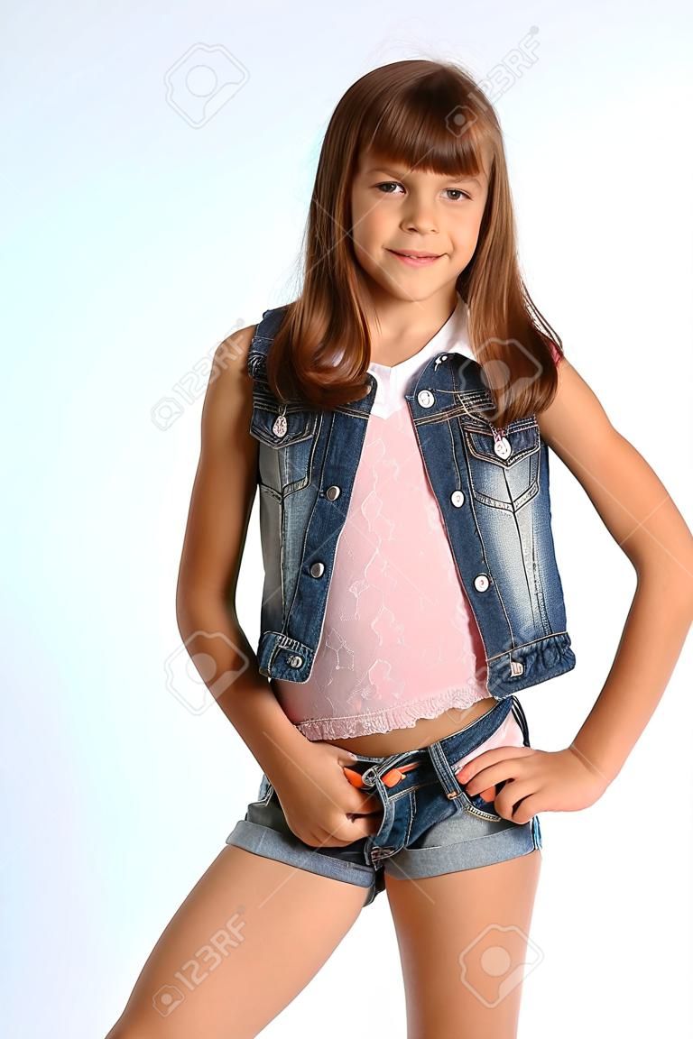 Retrato de uma menina bonita em um shorts denim está de pé. Criança atraente elegante com um corpo esbelto e pernas longas em meia-calça. A jovem estudante tem 9 anos de idade.