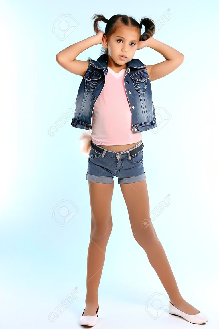 Mooi meisje in een denim short staat op volle lengte. Elegant aantrekkelijk kind met een slank lichaam en lange benen in panty. Het jonge schoolmeisje is 9 jaar oud.