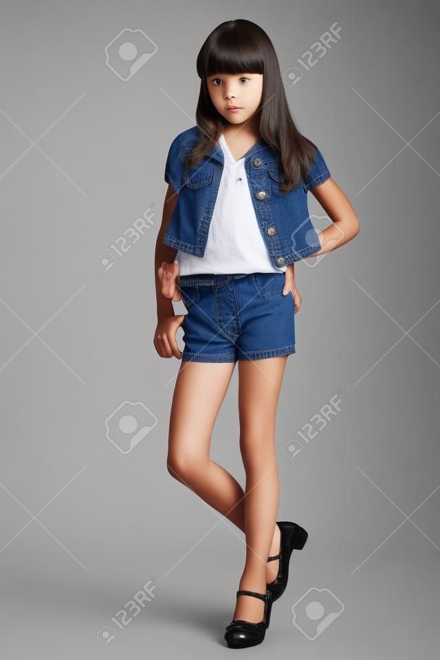 Hermosa chica en pantalones cortos de mezclilla está de pie en toda su longitud. Niño elegante y atractivo con un cuerpo delgado y piernas largas en pantimedias. La joven colegiala tiene 9 años.