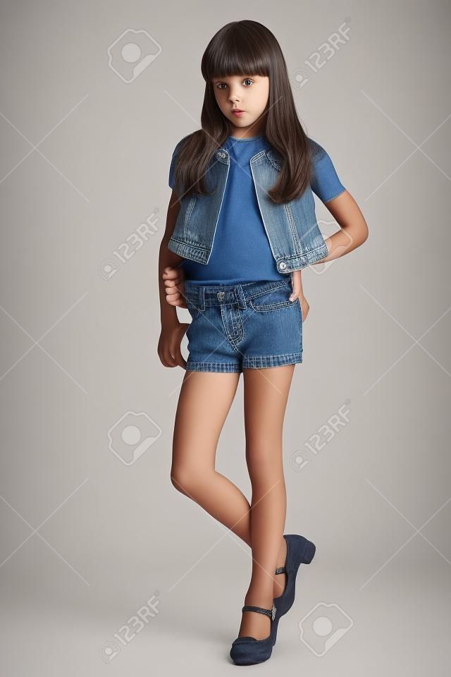 데님 반바지에 아름다운 소녀가 전체 길이로 서 있습니다. 날씬한 몸매와 긴 다리를 가진 우아한 매력적인 아이. 어린 여학생은 9 살입니다.