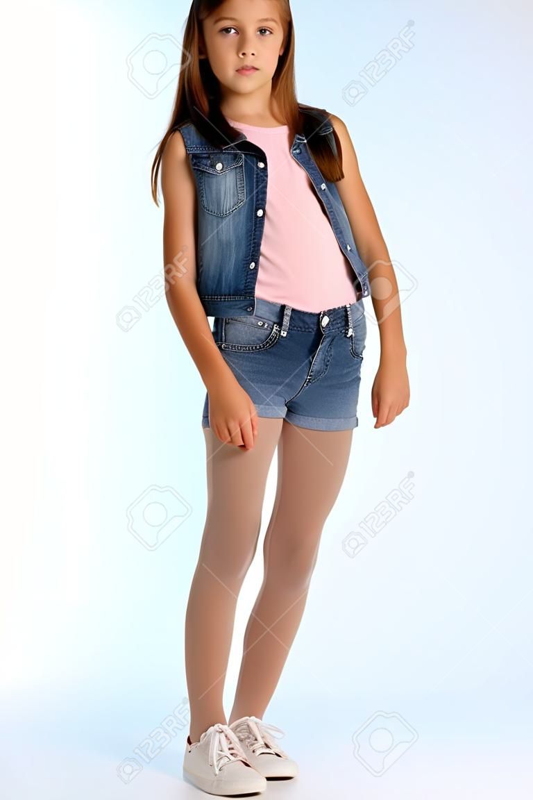 Красивая девушка в джинсовых шортах стоит в полный рост. Элегантный привлекательный ребенок со стройным телом и длинными ножками в колготках. Юной школьнице 9 лет.