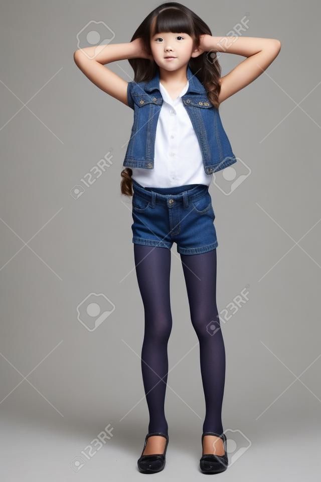 牛仔短裤的美丽的女孩站立在全长。优雅诱人的孩子，苗条的身材，连裤袜长腿。年轻的女学生9岁。
