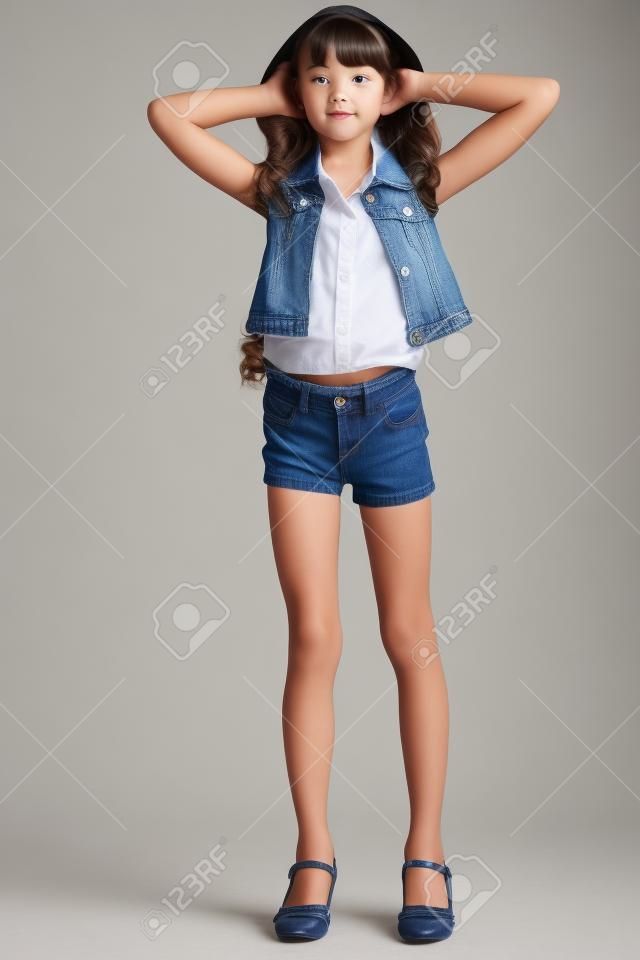 Kot şortlu güzel kız tam uzunlukta duruyor. İnce bir vücuda ve külotlu çorapla uzun bacaklara sahip zarif çekici çocuk Genç kız öğrenci 9 yaşında.