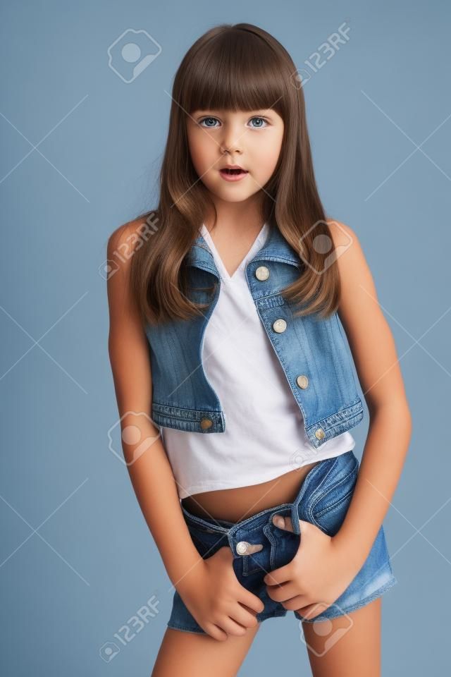 Das Porträt eines schönen Mädchens in einer Jeansshorts steht. Elegantes attraktives Kind mit einem schlanken Körper und langen Beinen in Strumpfhosen. Das junge Schulmädchen ist 9 Jahre alt.