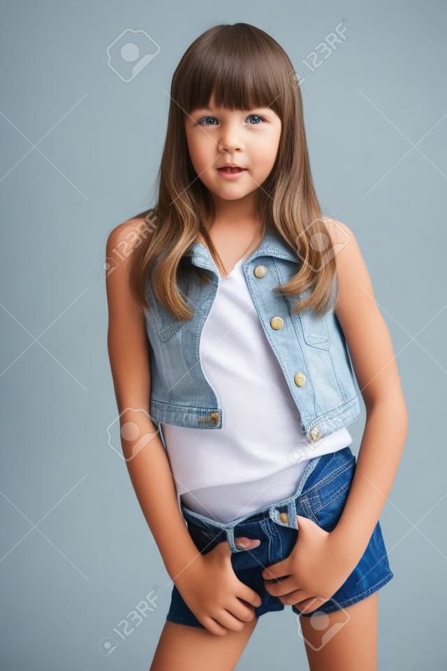 Das Porträt eines schönen Mädchens in einer Jeansshorts steht. Elegantes attraktives Kind mit einem schlanken Körper und langen Beinen in Strumpfhosen. Das junge Schulmädchen ist 9 Jahre alt.