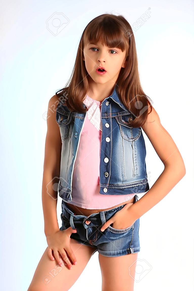 Portrait of a beautiful girl in a denim shorts is standing. Elegant attractive child with a slender body and long legs in pantyhose. The young schoolgirl is 9 years old.