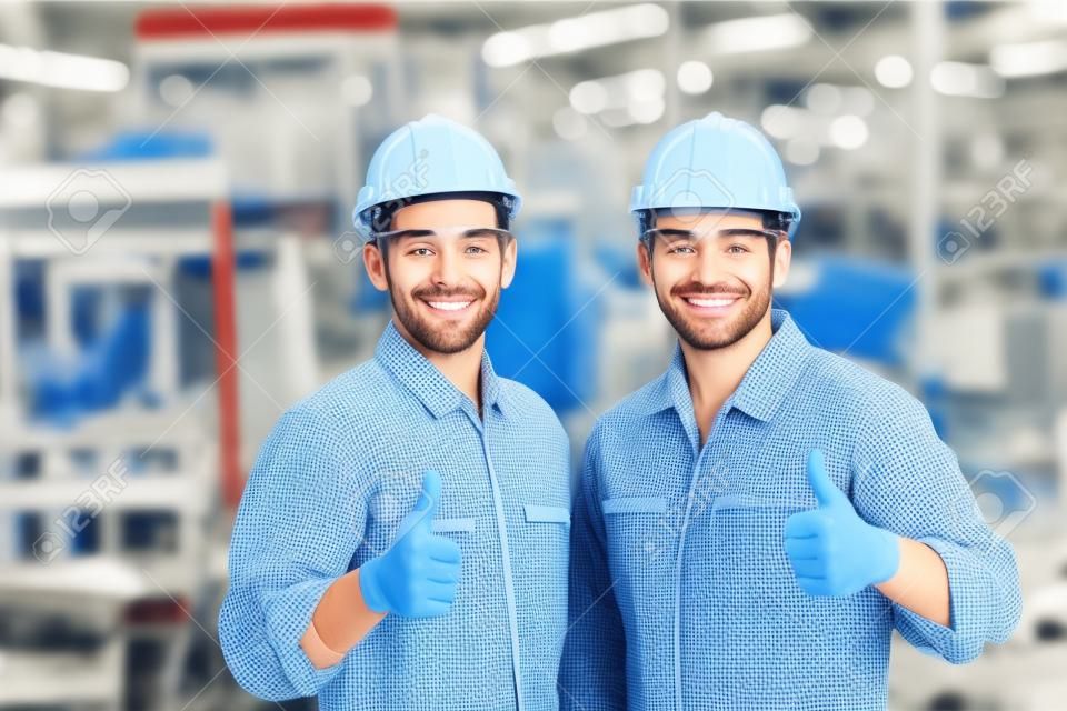 幸せな労働者チームは、工場で良い仕事のために親指を見せる手を微笑んでいます。