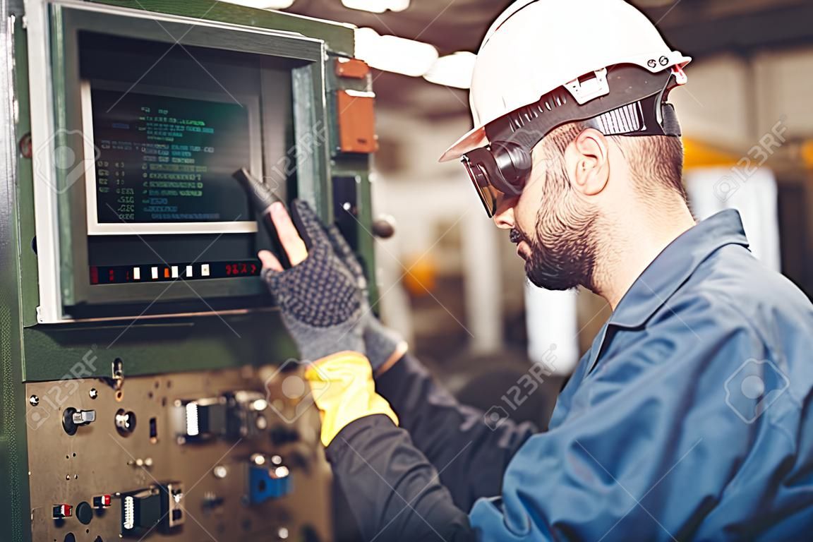El trabajador opera la máquina CNC con monitor de código G, industria de trabajo de alta calificación con ropa de seguridad.