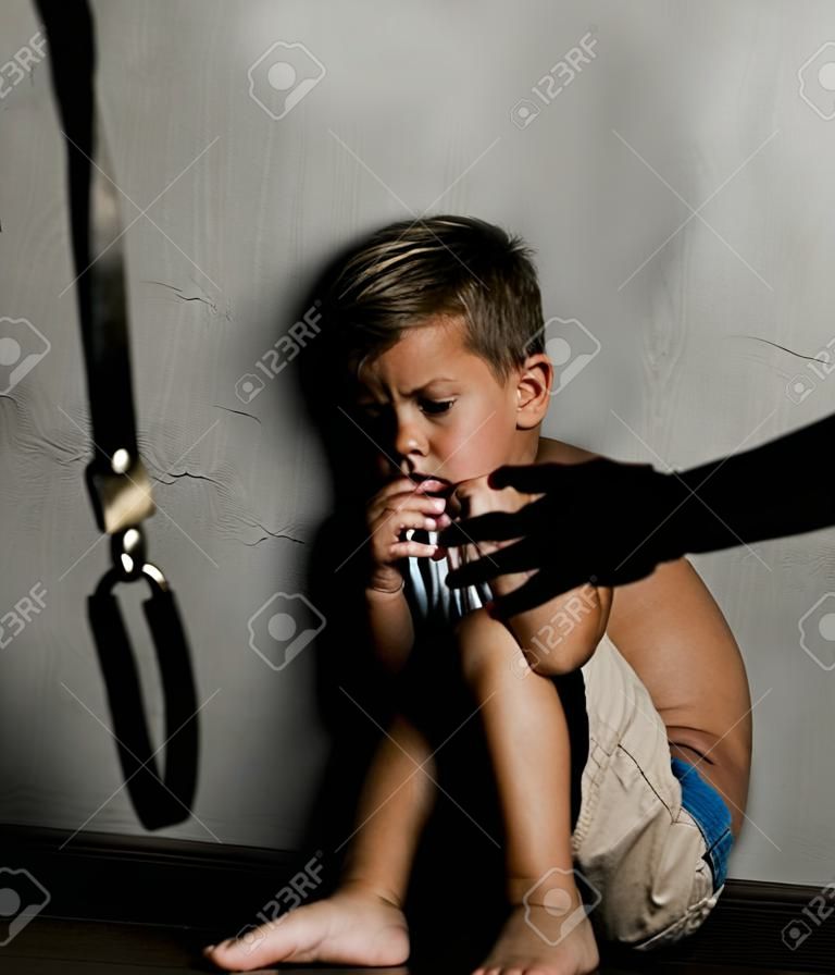 Violencia doméstica: la mano del padre con el cinturón y el hijo espantado golpeado.