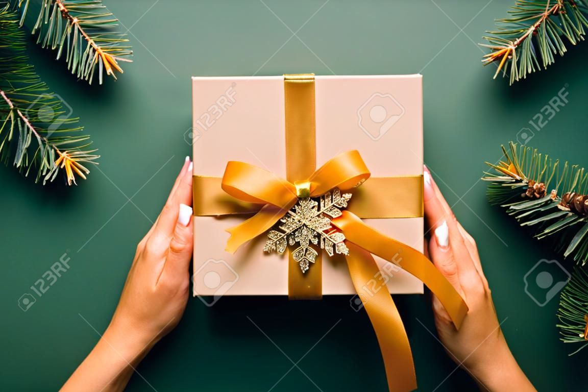 Vintage Weihnachtsgeschenkbox mit goldener Schleife und Schneeflocke auf dunkelgrünem Hintergrund mit Tannenzweigen. Weihnachtsgeschenk im Retro-Stil, Neujahrsüberraschung.