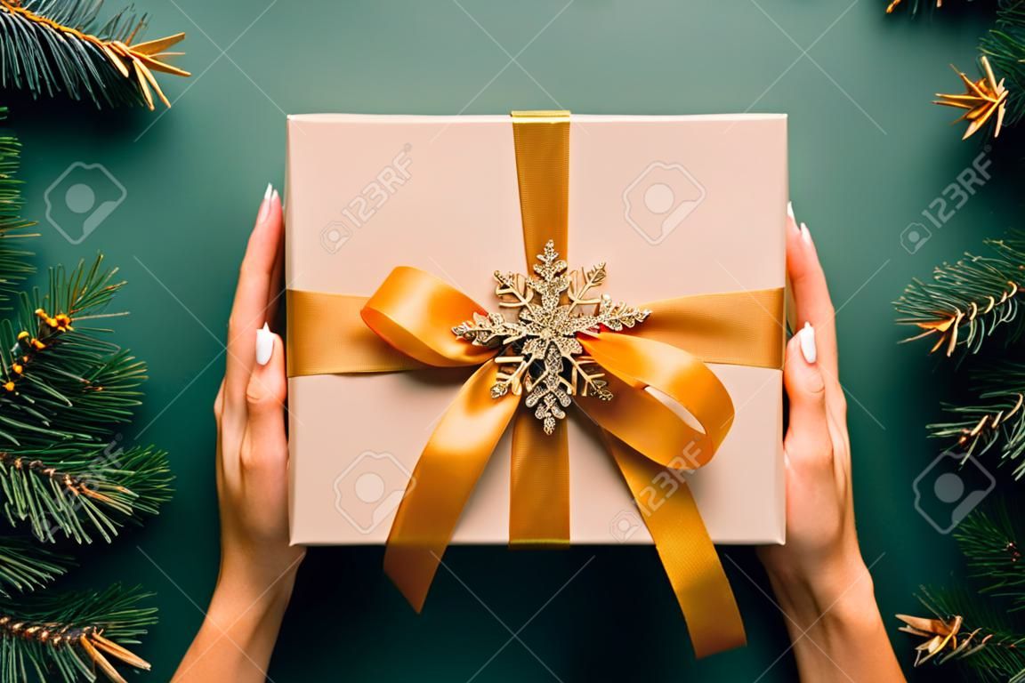 Vintage kerstcadeau doos met gouden lint strik en sneeuwvlok op donker groene achtergrond met dennenboom takken. Retro stijl Kerstmis aanwezig, Nieuwjaar verrassing.