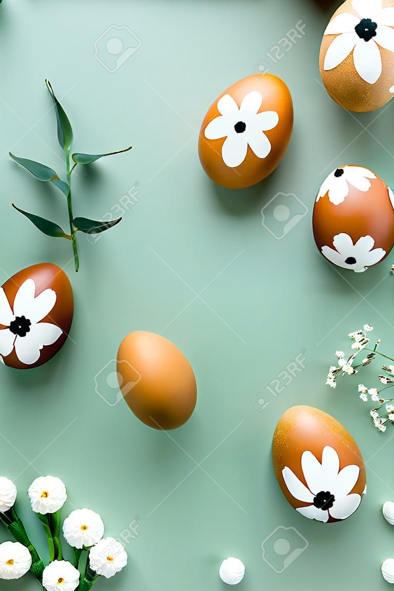 Marco de huevos de Pascua y flores sobre fondo verde pastel. Feliz maqueta de banner vertical de Pascua. Plano, vista superior, espacio de copia.