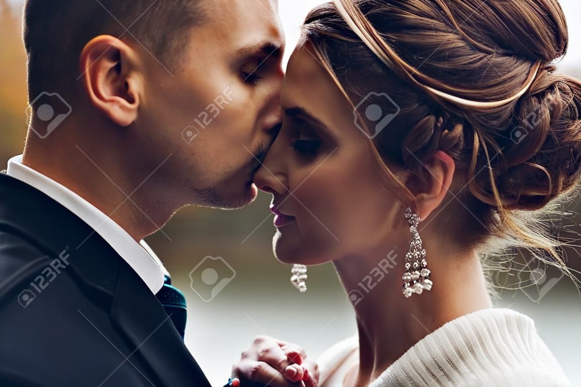 Noivo beijando noiva bonita na testa. Casamento de outono.