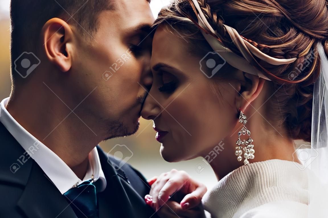 Noivo beijando noiva bonita na testa. Casamento de outono.
