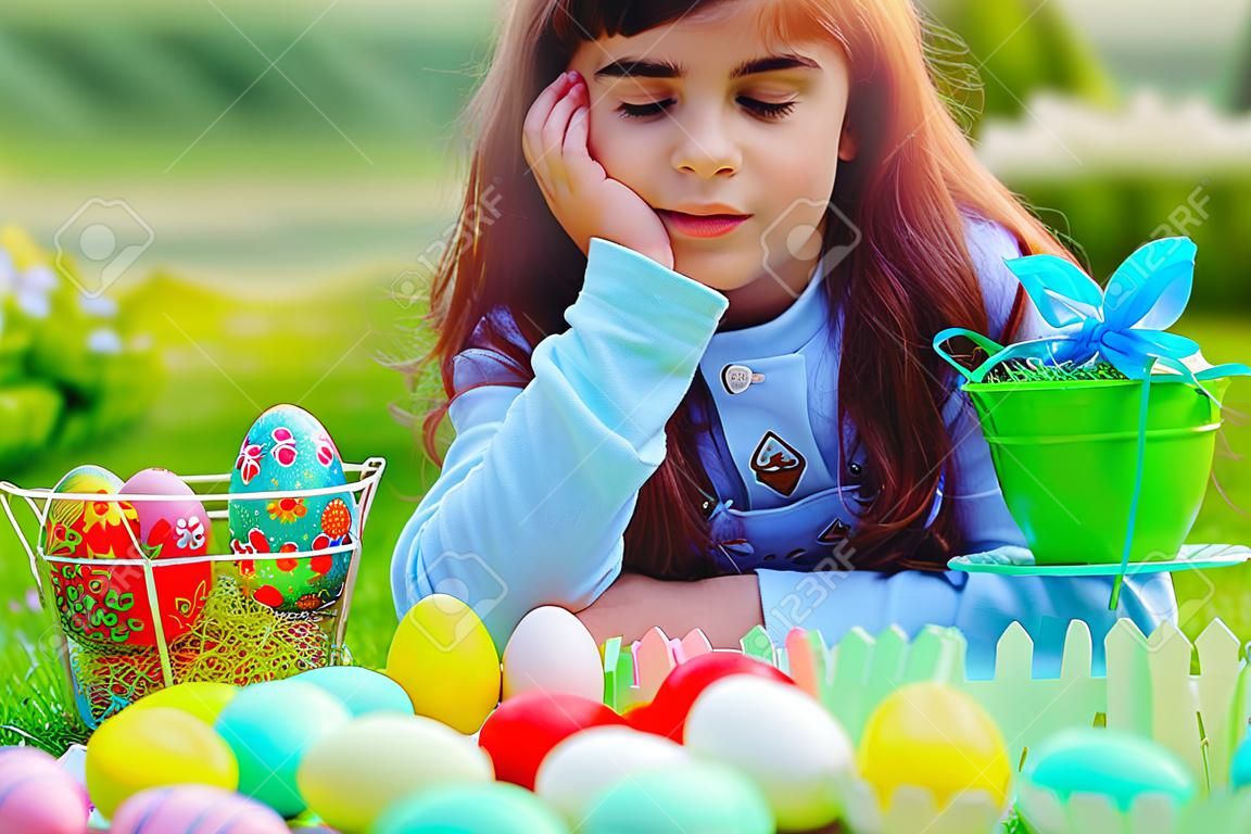 Cute little girl playing with colorful Easter eggs outdoors in the yard, happy festive play, enjoying traditional Easter eggs hunting