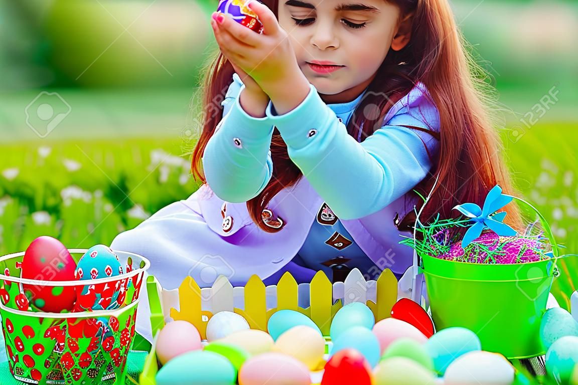 Jolie petite fille jouant avec des oeufs de Pâques colorés à l'extérieur dans la cour, jeu festif heureux, profitant de la chasse traditionnelle aux oeufs de Pâques