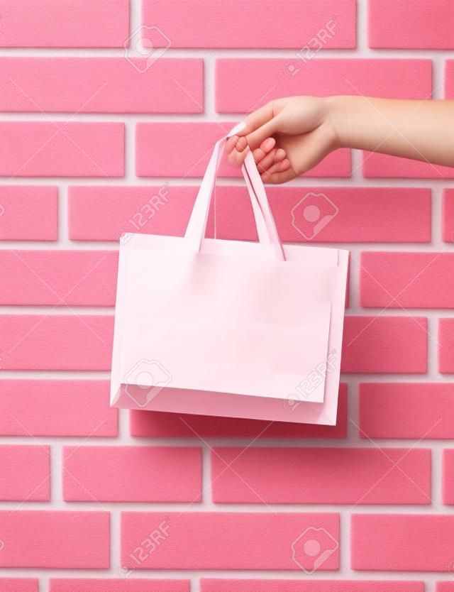 light pink color paper shopping bag or package in female hand as holiday present or gift on brick wall background, copy space