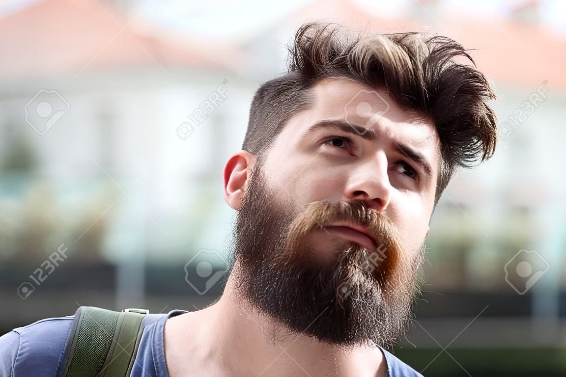 Hipster with beard and mustache on strict face looks at sky, urban background, defocused. Bearded guy enjoy sunny weather. Man with beard looks at sky on sunny day. Weather forecast concept