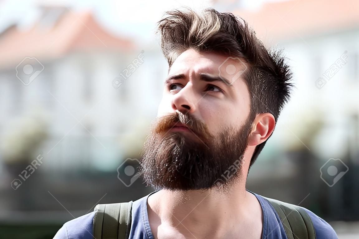 Hipster with beard and mustache on strict face looks at sky, urban background, defocused. Bearded guy enjoy sunny weather. Man with beard looks at sky on sunny day. Weather forecast concept