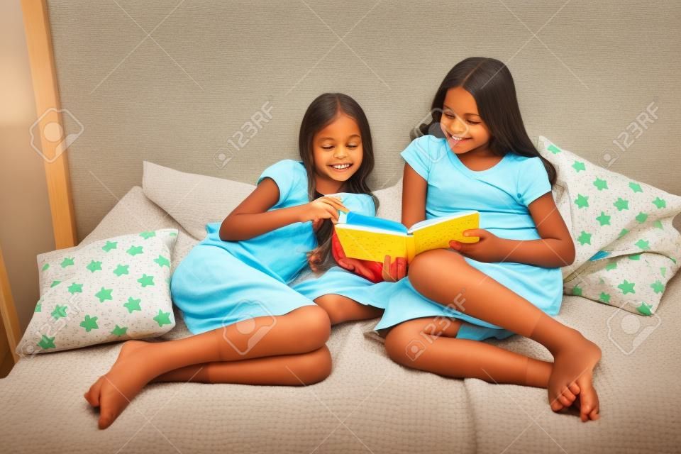 Children read book in bed. Family tradition. Girls best friends read fairy tale before sleep. Best books for kids. Reading before bed can help sleep better at night. Stories every kid should read.