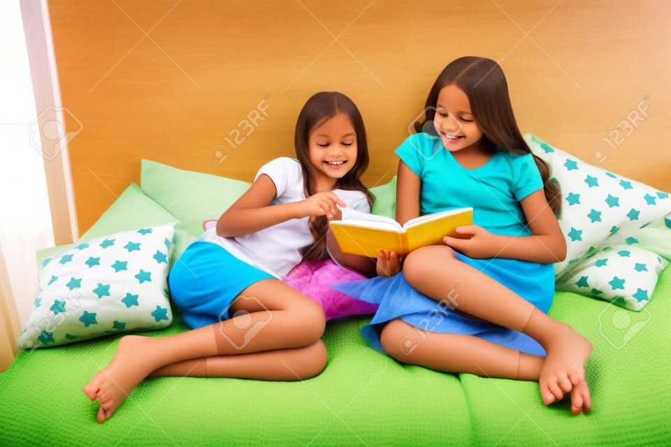 Children read book in bed. Family tradition. Girls best friends read fairy tale before sleep. Best books for kids. Reading before bed can help sleep better at night. Stories every kid should read.