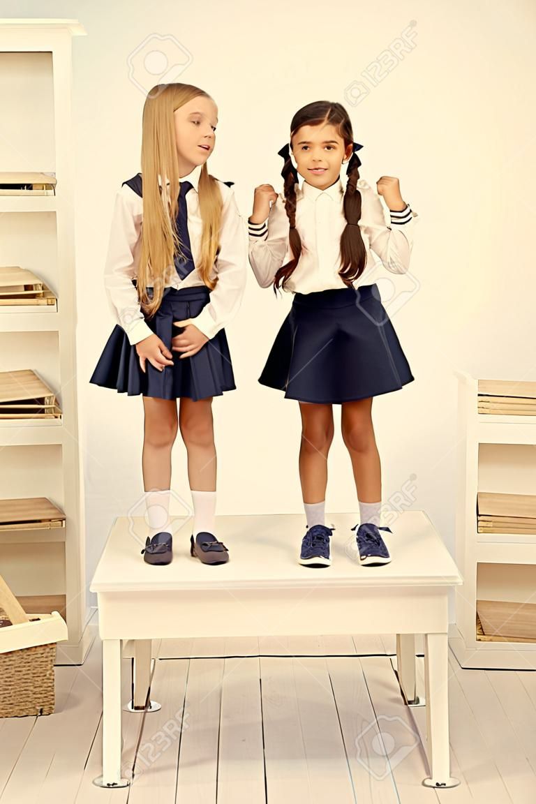 Back to school style. Happy small girls with long hair styles standing on desk in class. Little children smiling in school style. Giving school fashion a sense of style