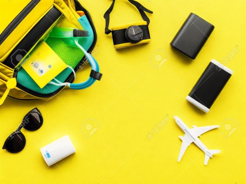 Vista dall'alto o disposizione piatta degli accessori da viaggio con maschera medica e spray alcolico nello zaino su sfondo giallo. Viaggiare durante la pandemia e la nuova normalità.